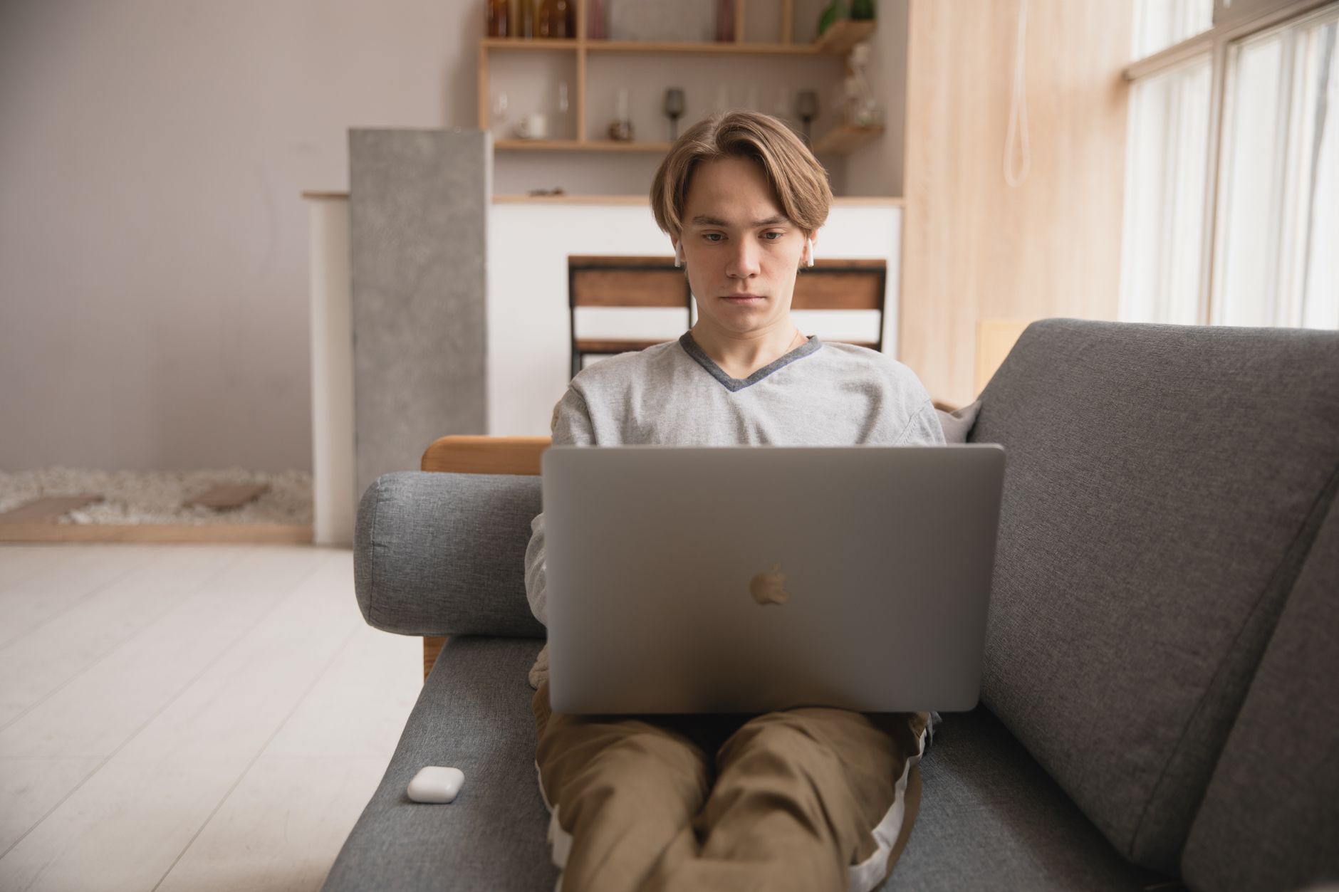 Jovem sentado num sofá a trabalhar num portátil, num ambiente doméstico acolhedor.